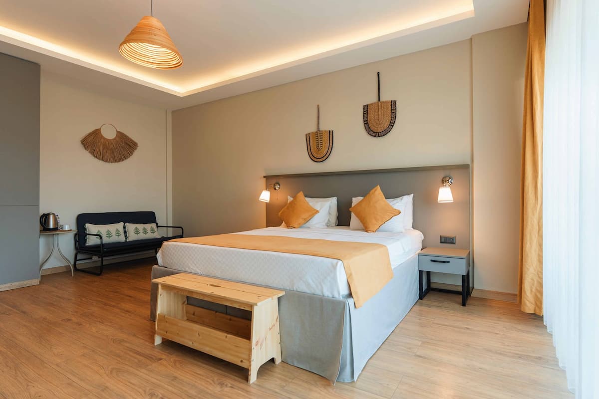 A modern hotel room with a large bed, bedside tables, a bench, and a sofa.