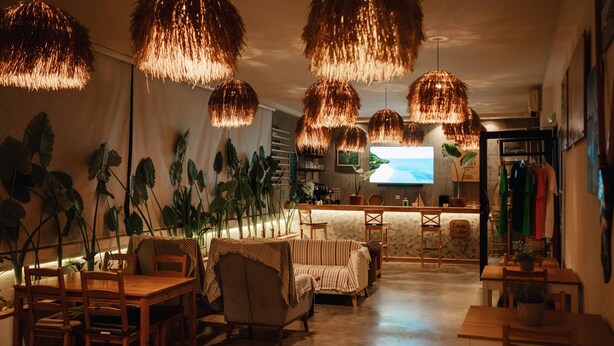 Un restaurante acogedor con muebles de madera, luces colgantes y una pantalla de televisión que muestra una escena de playa.