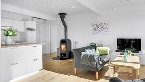 A modern living room with a sofa, a TV, a small table, and a kitchen area with cabinets and a stove. - 4 bedroom awesome home in Dronningmølle (Dronningmølle)