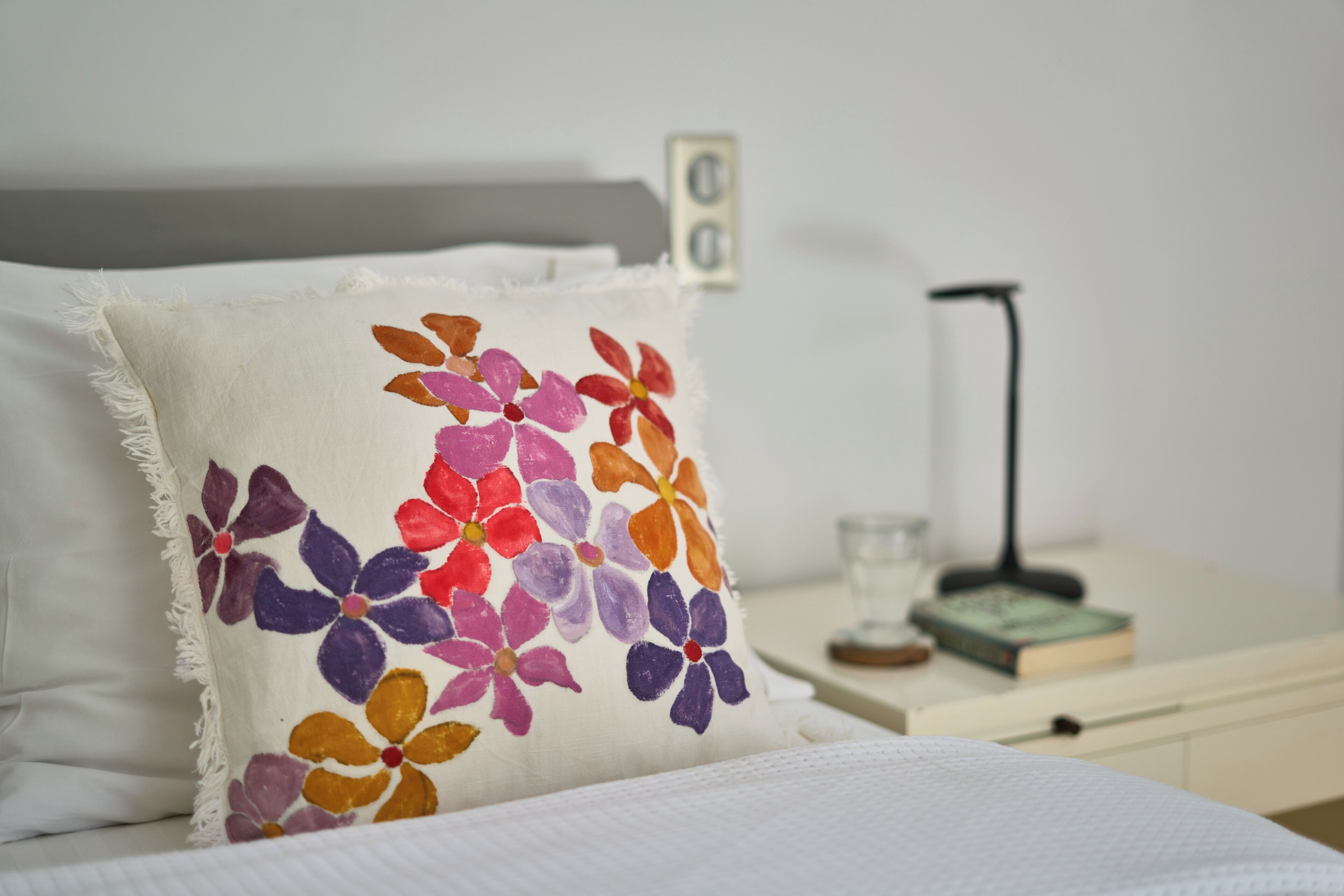 A bed with a white pillow and a colorful floral pillow.