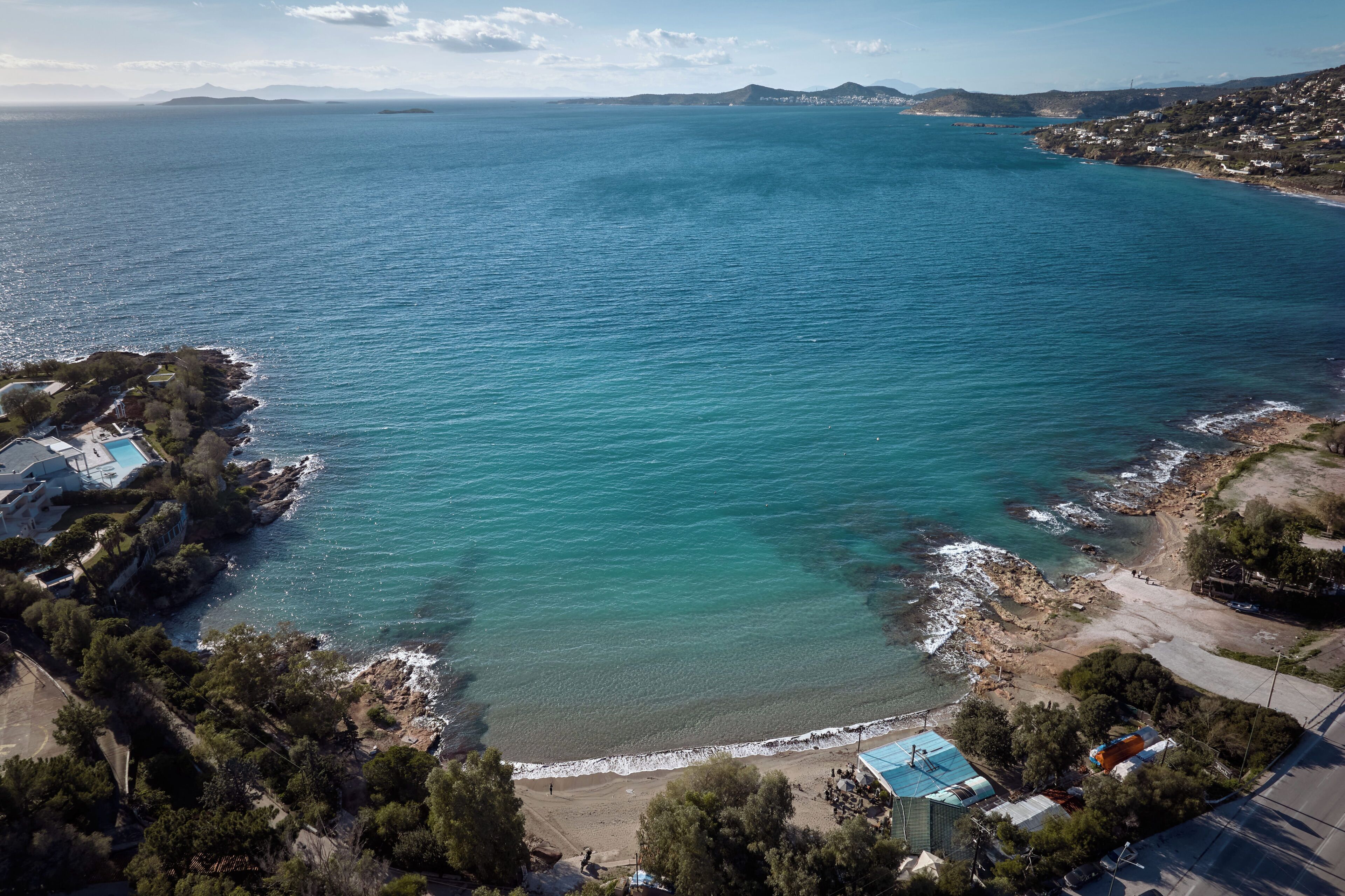 Oversigtsbillede af et kystområde med en strand, klippefyldt kystlinje og bygninger med blå tage.