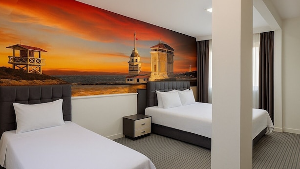 A hotel room with two beds, a nightstand, and a mural of a sunset cityscape. - Acar Airport Hotel Plus (Arnavutköy)