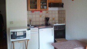 Een kleine keuken met een magnetron, koelkast, fornuis en houten kastjes.