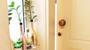 Un couloir avec une porte blanche, un miroir qui reflète une plante et une plante en pot posée sur le sol.