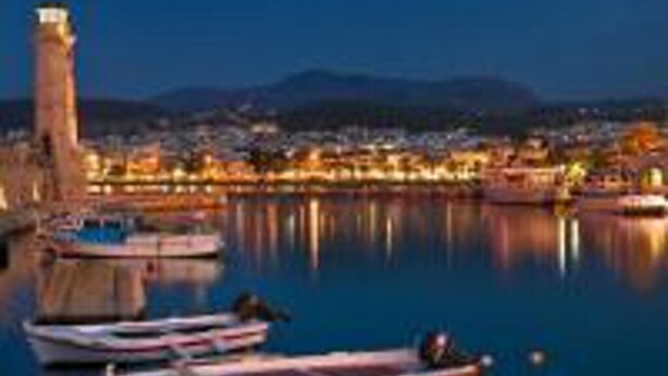 Un port au crépuscule, avec des bateaux amarrés, une tour imposante et une vue sur la ville en arrière-plan.