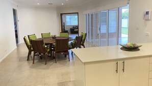 Un comedor con mesa y sillas, una encimera de cocina y un ventanal corredero que da a un espacio exterior.