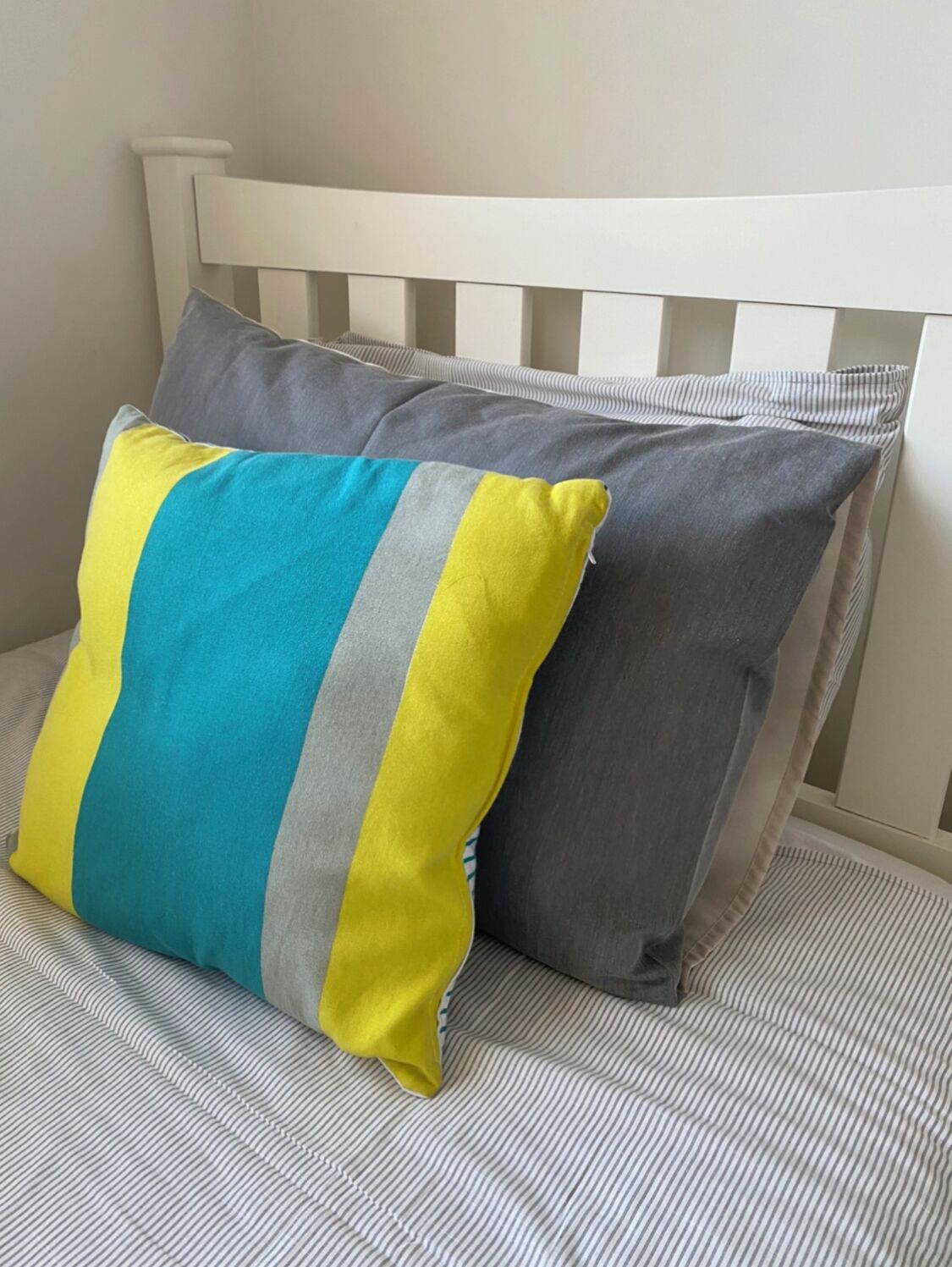 A bed with striped bedding and two pillows, one with a multicolored design and the other plain.