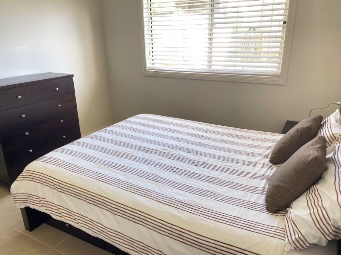 Een slaapkamer met een bed, een dressoir en een raam met jaloezieën.