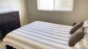 Een slaapkamer met een bed, een dressoir en een raam met jaloezieën.