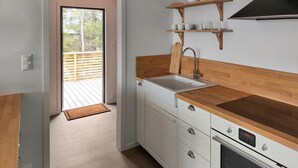 Una cocina con encimera de madera, armarios blancos, horno empotrado y ventana con vistas a una terraza.