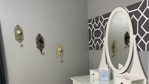 A room with a grey wall, a white vanity with a mirror, and three decorative wall pieces. - Two bedroom Cottage (Cornell)