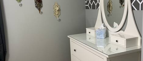 A room with a grey wall, a white vanity with a mirror, and three decorative wall pieces.