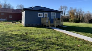A small, single-story building with a wooden deck and a stone foundation. - Two bedroom Cottage (Cornell)
