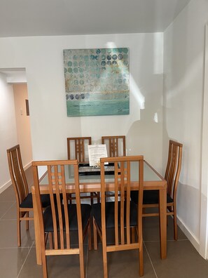 Uma área de refeições com mesa e cadeiras de madeira, um quadro decorativo na parede e piso de azulejos.