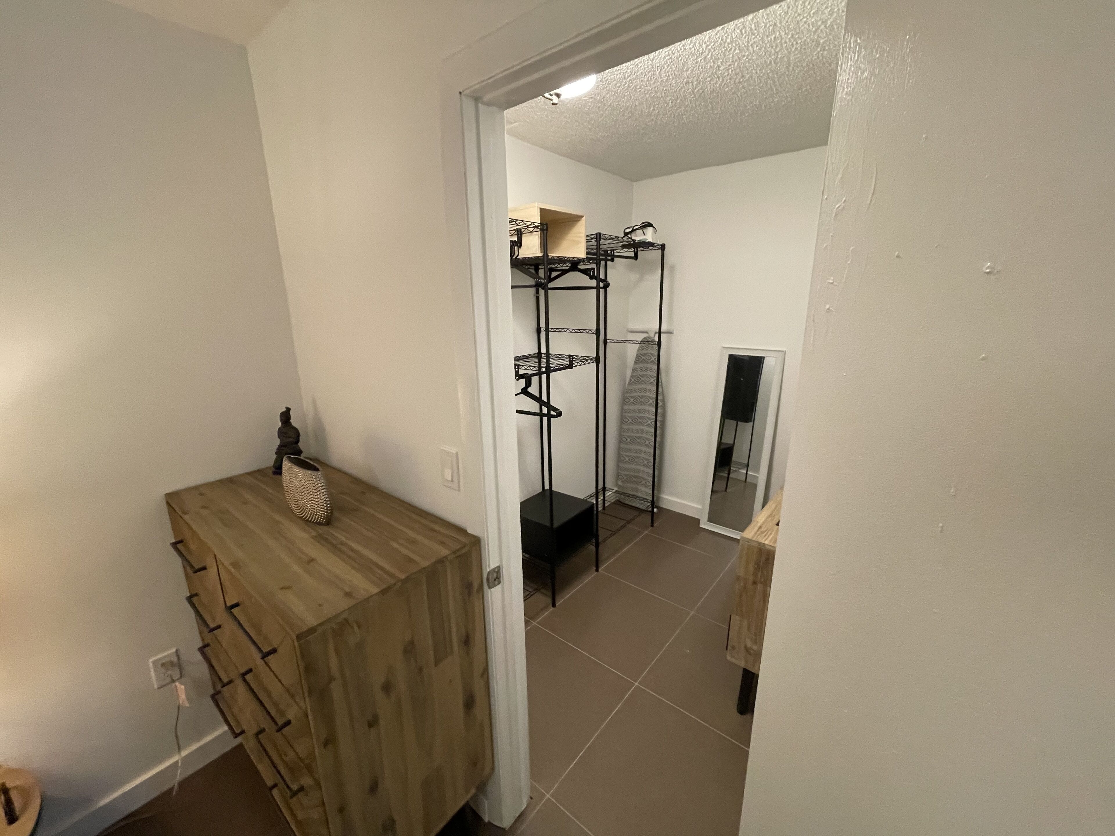 Un couloir avec une armoire en bois, un étagère en métal et un miroir accroché au mur.