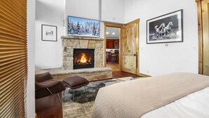A bedroom with a stone fireplace, a bed, a leather chair, and a dining area visible through an open door. - 502 A Gold Coast! 3 Bedroom Townhouse by RedAwning (Park City)