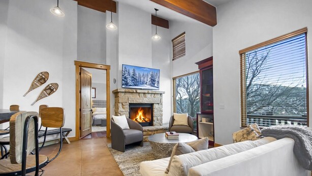 A spacious living room with a fireplace, a dining area with chairs, a sofa, and a large window offering a view of the outdoors. - 502 A Gold Coast! 3 Bedroom Townhouse by RedAwning (Park City)