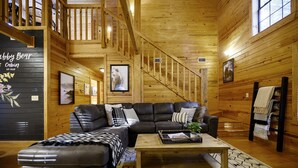 Ein Blockhaus-Interieur mit einer Holztreppe, einer Couch, einem Couchtisch und einem Kamin.