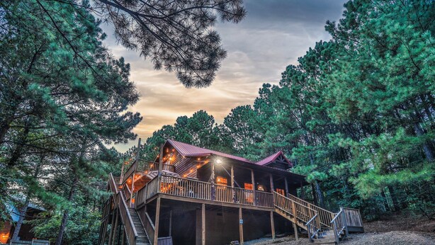 Eine Holzhütte mit Terrasse und Treppe, umgeben von Bäumen.