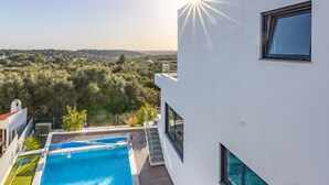 Un edificio moderno con piscina, ampie finestre e vista su un paesaggio collinare.