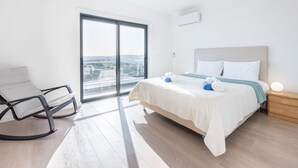 Una camera d'albergo moderna con un letto grande, una zona salotto con una poltrona e vista panoramica da una finestra ampia.