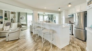 Amplia sala de estar con una isla central, taburetes blancos, un sofá y una mesa de comedor.
