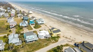 Vista aérea de una zona residencial costera con casas a lo largo de la playa, cielo despejado y el océano al fondo.