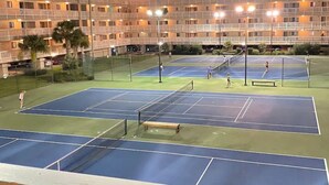 An outdoor tennis court surrounded by a multi-story hotel building with balconies.
