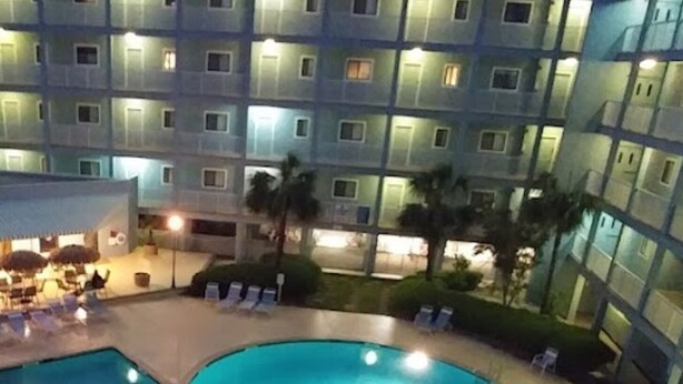 A swimming pool with lounge chairs and umbrellas, surrounded by a building with multiple balconies and windows.