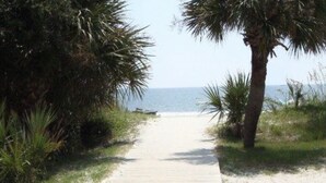 A wooden boardwalk leading to a sandy beach with palm trees and the ocean in the background.