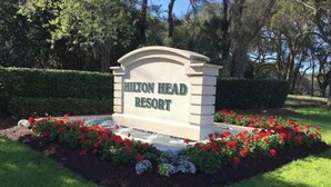 A sign for Hilton Head Resort surrounded by a landscaped garden with red flowers.