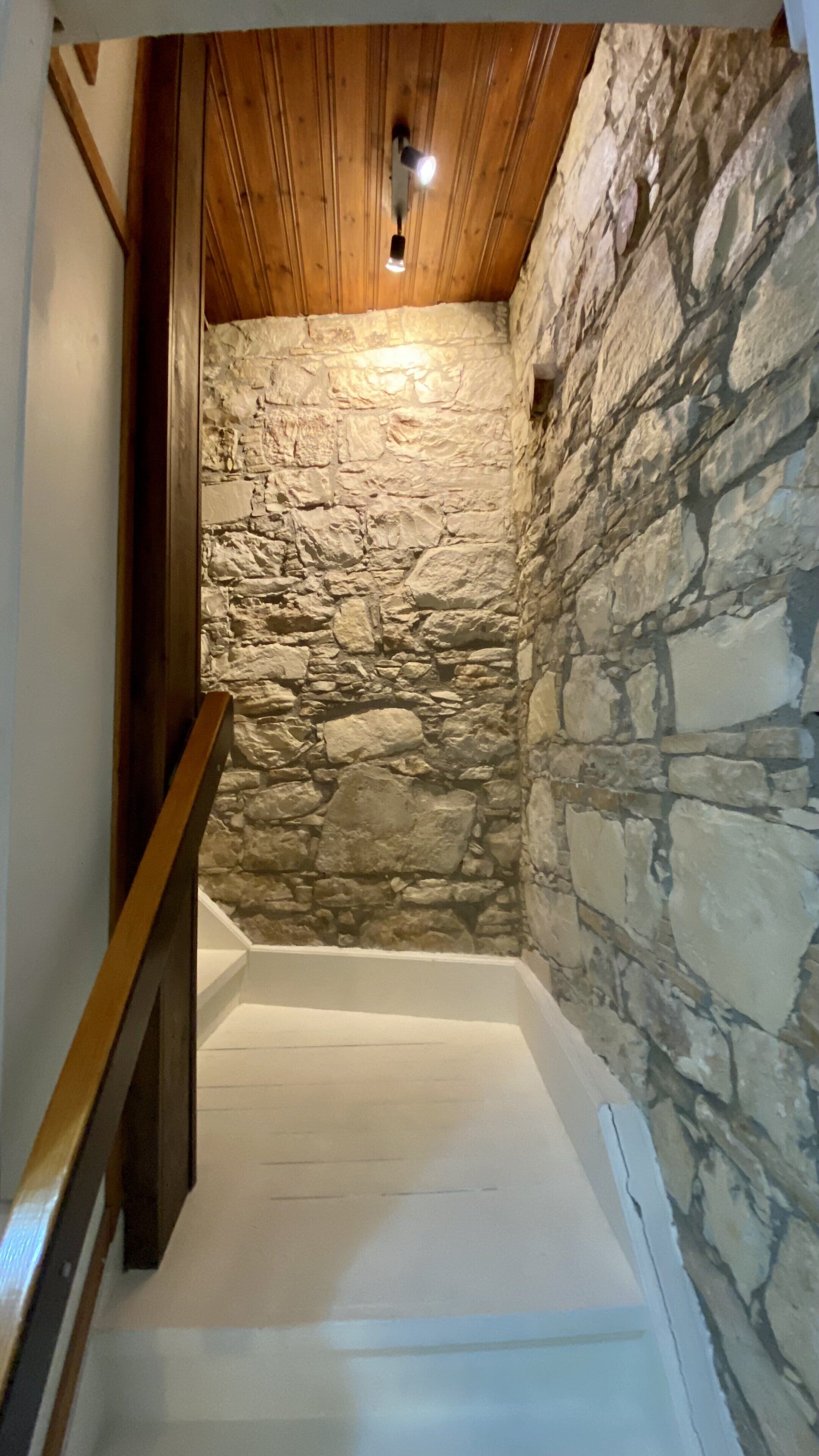 A narrow staircase with stone walls and wooden beams, leading to a lower level.