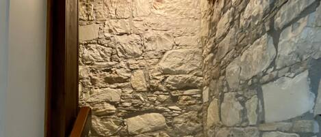 A narrow staircase with stone walls and wooden beams, leading to a lower level.