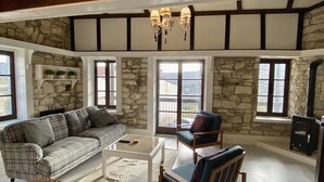 A cozy room with a stone wall, a plaid sofa, a wooden chair, and a glass coffee table. - Leonys House by TrulyCyprus (Dhoros)