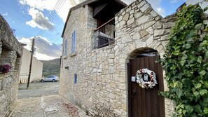 A stone building with a wooden door, a balcony, and a car parked in the background.