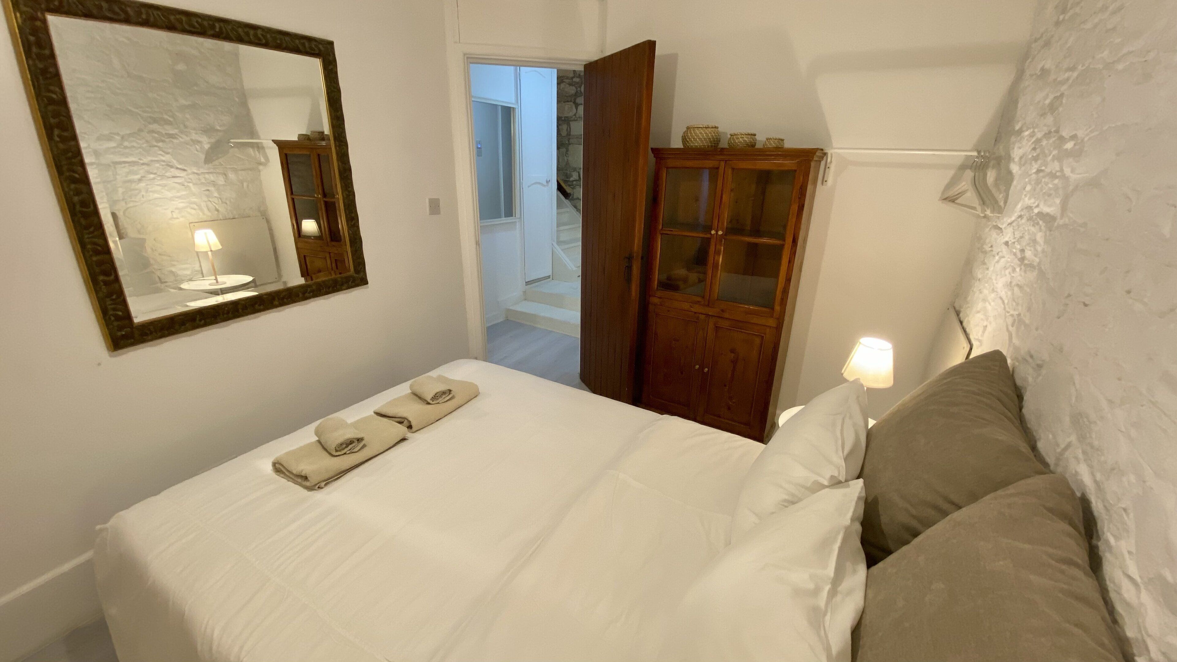 Een slaapkamer met een bed, een houten kast, een spiegel en een deur die leidt naar een trap.