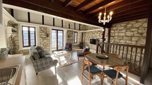 A spacious living area with a stone wall, a fireplace, a dining table with chairs, and a sofa. - Leonys House by TrulyCyprus (Dhoros)