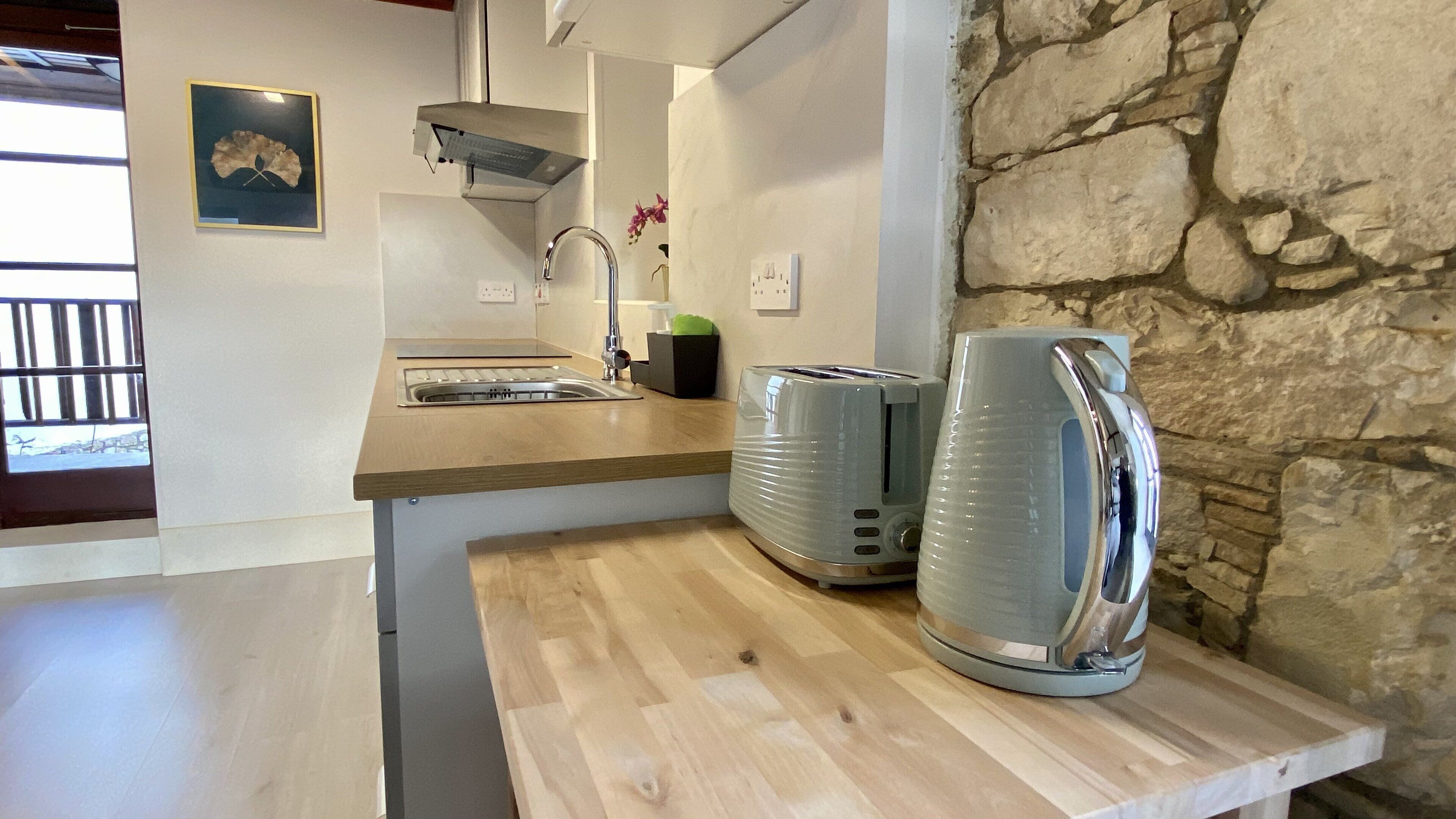 A kitchen with a stone wall, a wooden countertop, a sink, a toaster, and a vase with flowers.