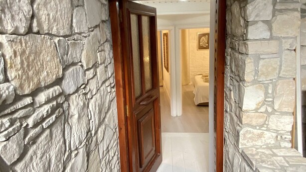A stone-walled hallway leading to a bedroom with a bed and a painting on the wall. - Leonys House by TrulyCyprus (Dhoros)