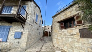 A narrow stone pathway leading to a building with a wooden door and a balcony. - Leonys House by TrulyCyprus (Dhoros)