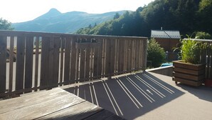 A wooden deck with a red umbrella, a wooden fence, and a view of mountains in the background. - Warm refuge for family vacations  (Saint-Jacques-des-Blats)