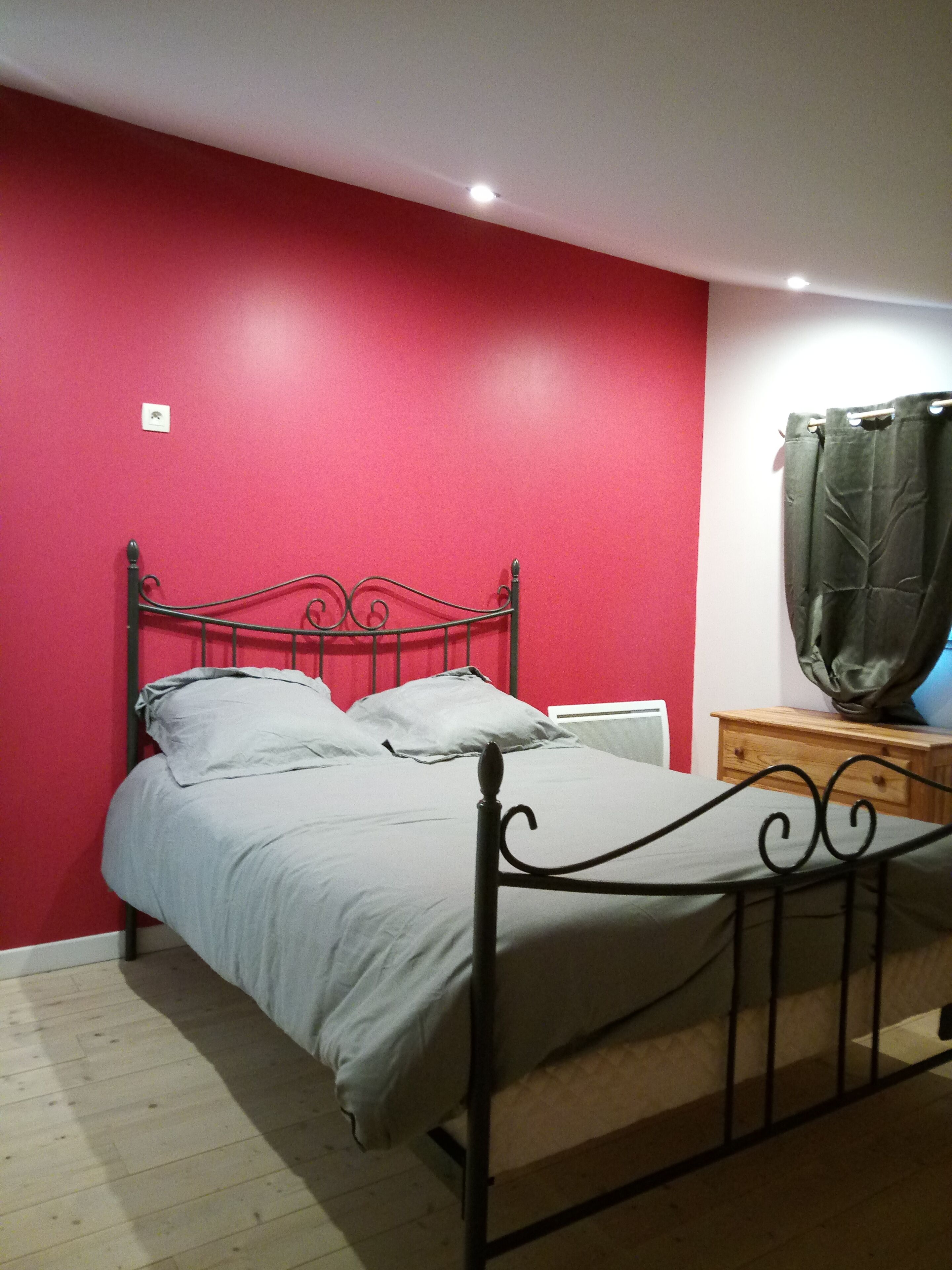Un lit simple avec un cadre en métal, dans une pièce aux murs rouges et au plancher en bois.