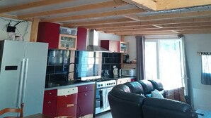 A kitchen with wooden cabinets, a refrigerator, a stove, and a dining area with a table and chairs. - Warm refuge for family vacations  (Saint-Jacques-des-Blats)