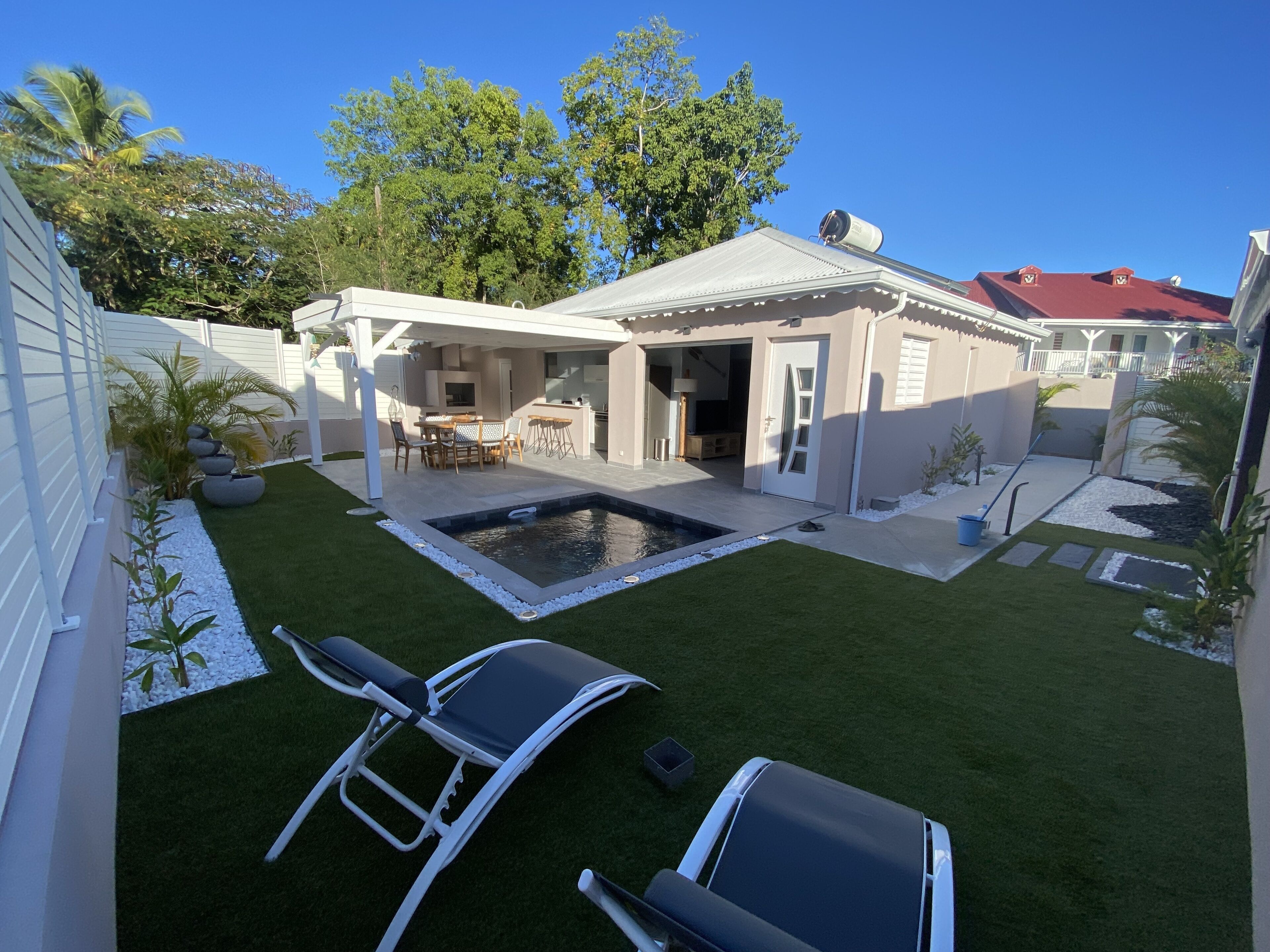 Un patio trasero con piscina, dos sillas de descanso, una mesa de patio y una zona de estar techada.