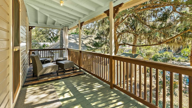 Une véranda couverte avec des balustrades en bois, un coin salon confortable et une vue sur un quartier résidentiel.