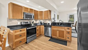 Une cuisine moderne avec des meubles en bois, des appareils électroménagers en acier inoxydable et un plan de travail noir.