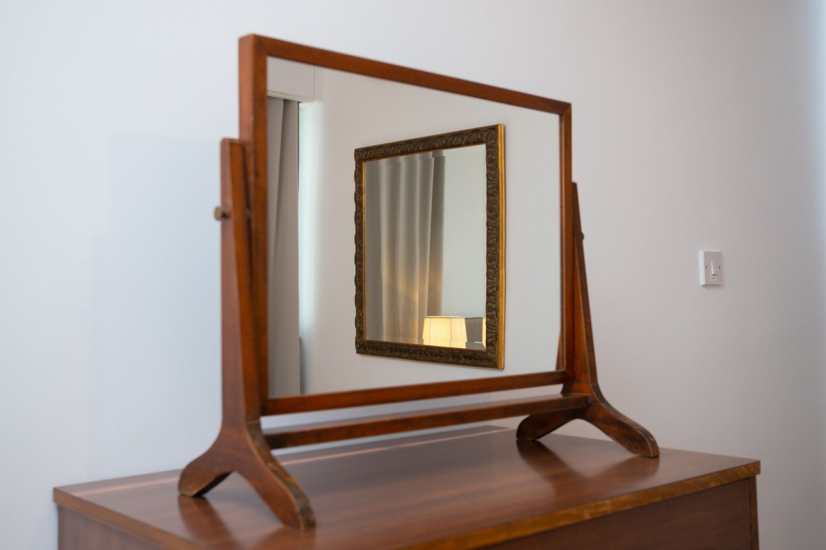 A wooden-framed mirror on a wooden dresser against a plain wall.