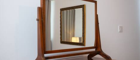 A wooden-framed mirror on a wooden dresser against a plain wall.
