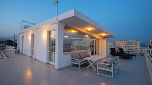 A modern rooftop terrace with a glass-enclosed seating area, a flagpole, and a view of the cityscape. - 1-80 Collection Penthouse by TrulyCyprus (Limassol)