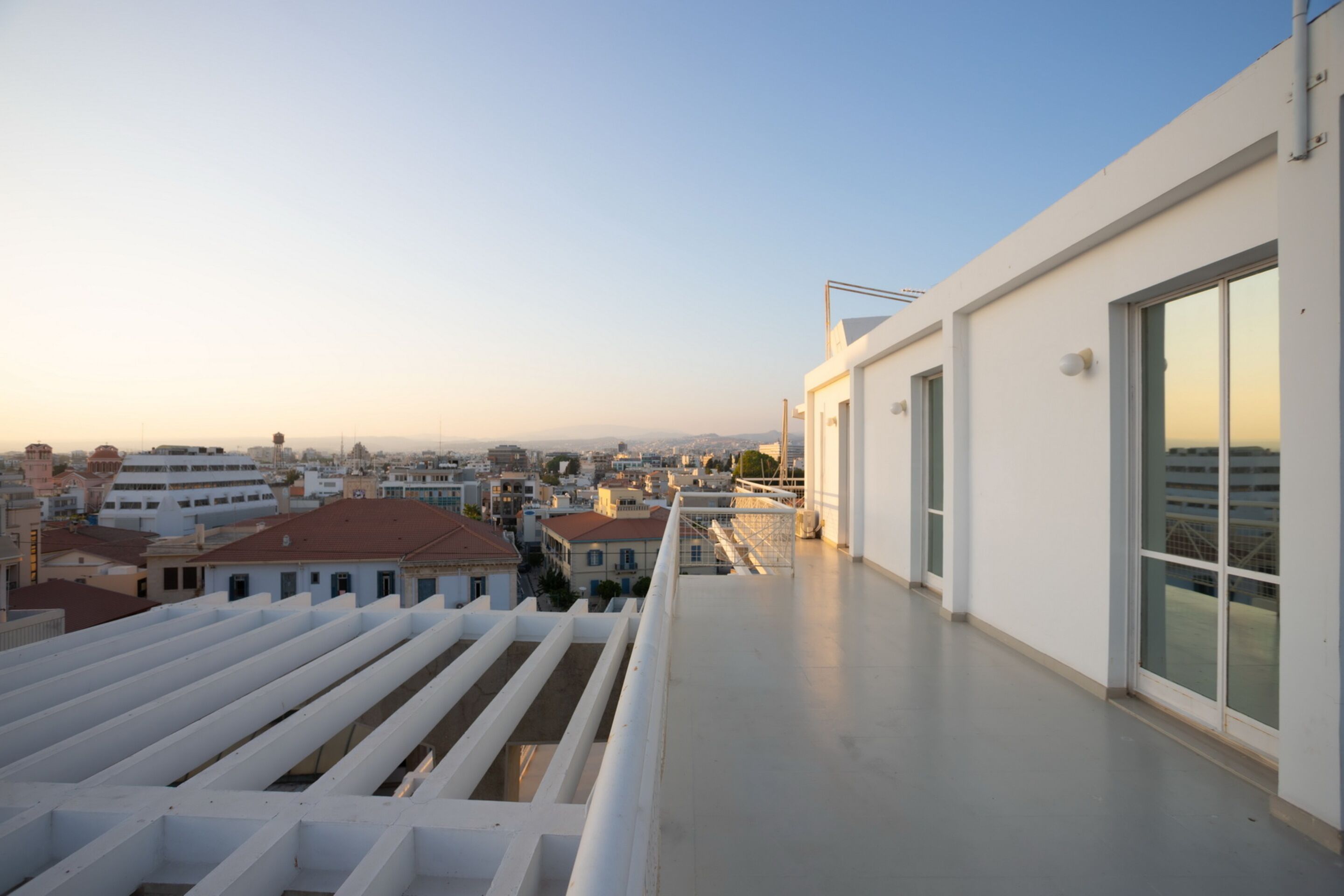 A rooftop terrace with a clear view of the cityscape, featuring modern buildings and a distant sunset.